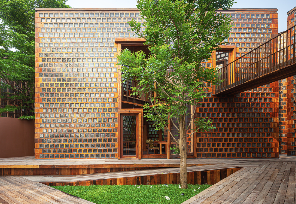 Building made from glass block and wood behind green tree.